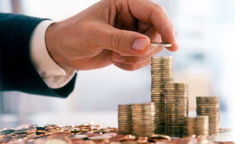 Main d'n homme qui empile des pièces de monnaie. Plusieurs tas de pièces sur la droite de l'image et beaucoup de pièces les unes sur les autres en bas de l'image.