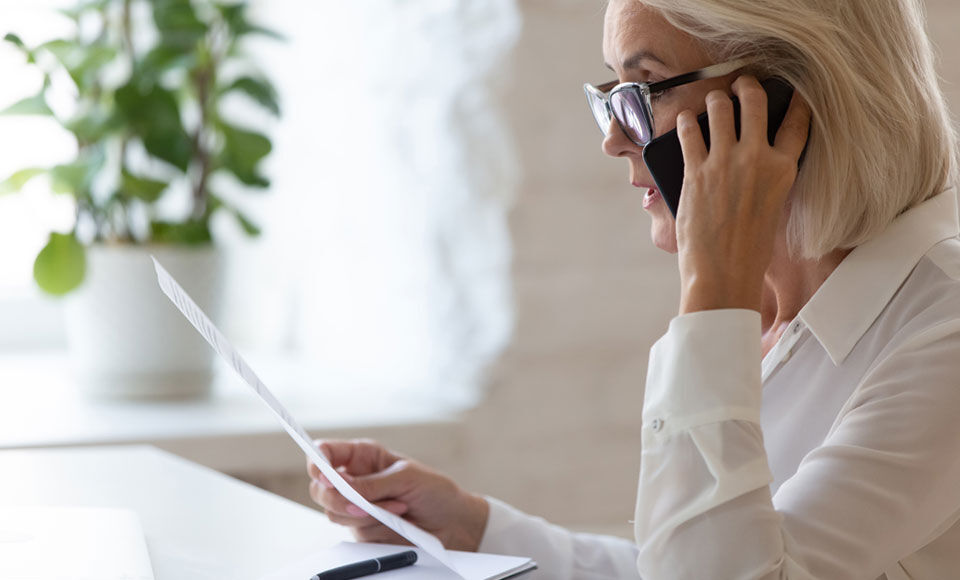 femme avec des lunettes en communication t&eacute;l&eacute;phonique qui lit un document papier