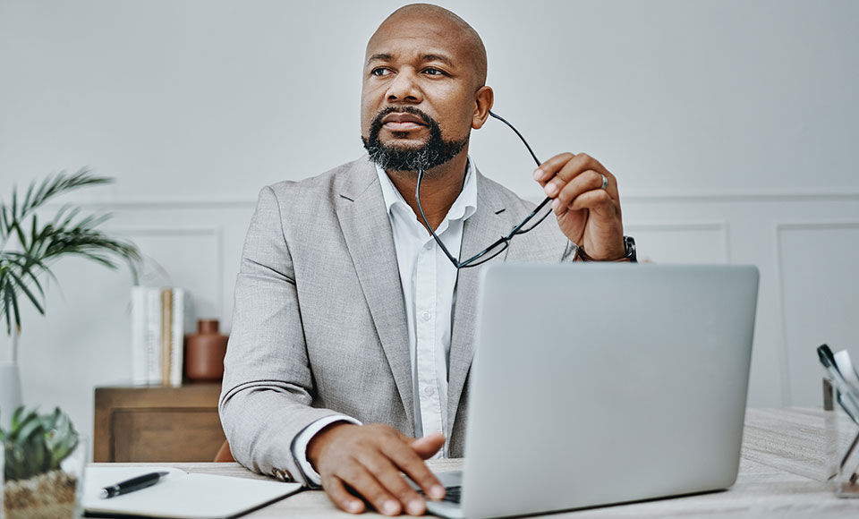 homme d'affaires assis &agrave; son bureau devant son ordinateur et tenant ses lunettes dans la main droite