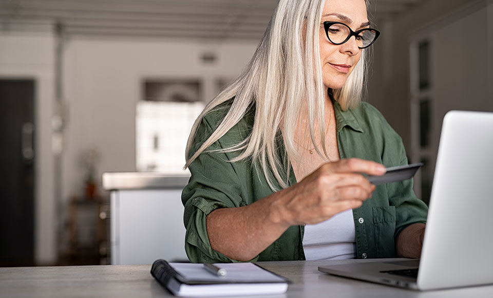 femme assise à son bureau devant son ordinateur effectuant un paiement en ligne avec sa carte