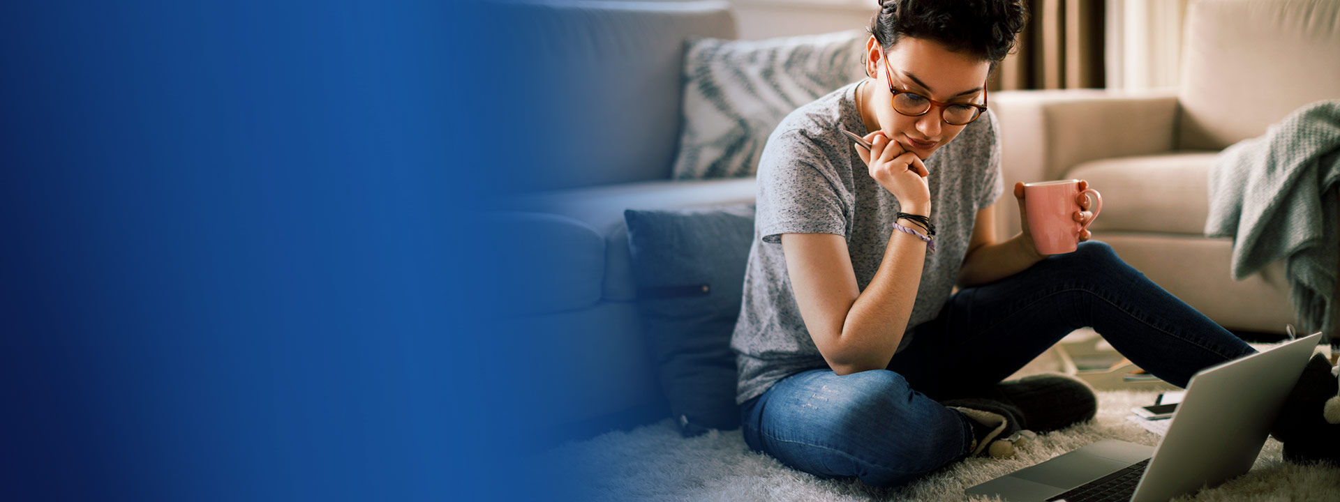 Jeune étudiante qui tient une tasse face à son ordinateur dans un appartement