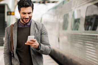 jeune homme souriant regardant un telephone dans une gare