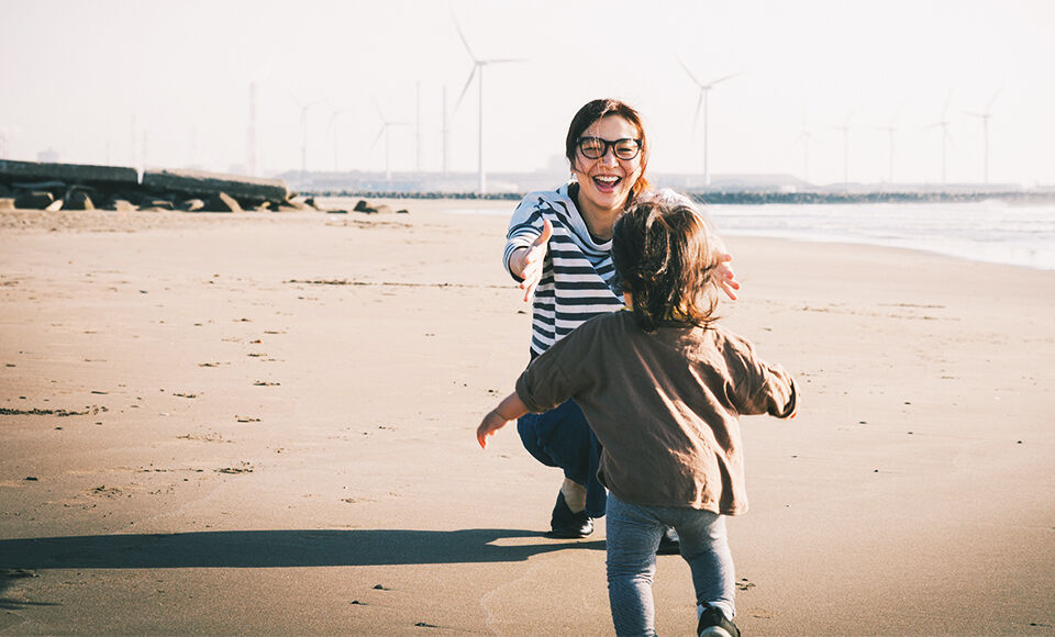Mere et fille jouant sur la plage devant des eoliennes