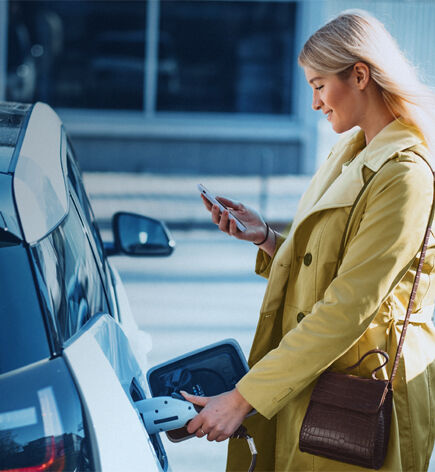 jeune femme chargeant voiture en regardant son smartphone