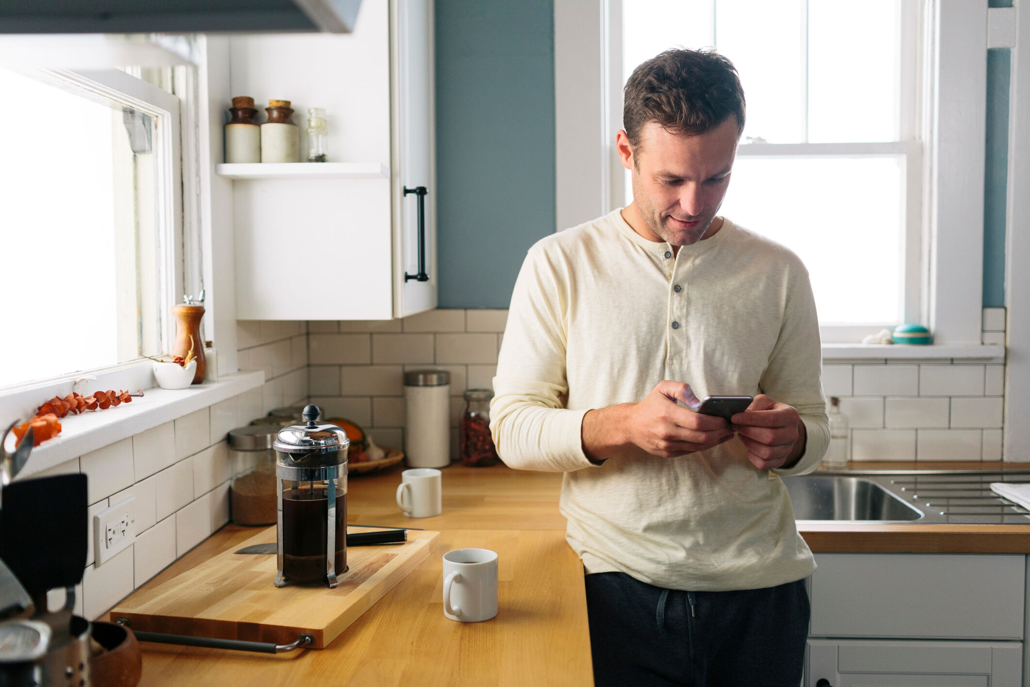 Homme utilisant un t&eacute;l&eacute;phone intelligent tout en se penchant par le comptoir de la cuisine &agrave; la maison