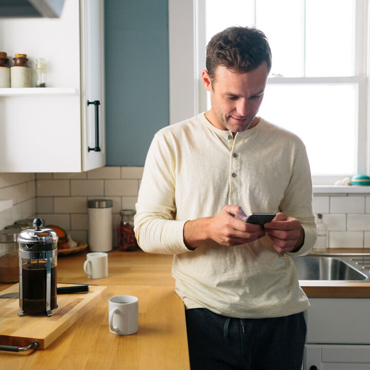 Homme utilisant un téléphone intelligent tout en se penchant par le comptoir de la cuisine à la maison