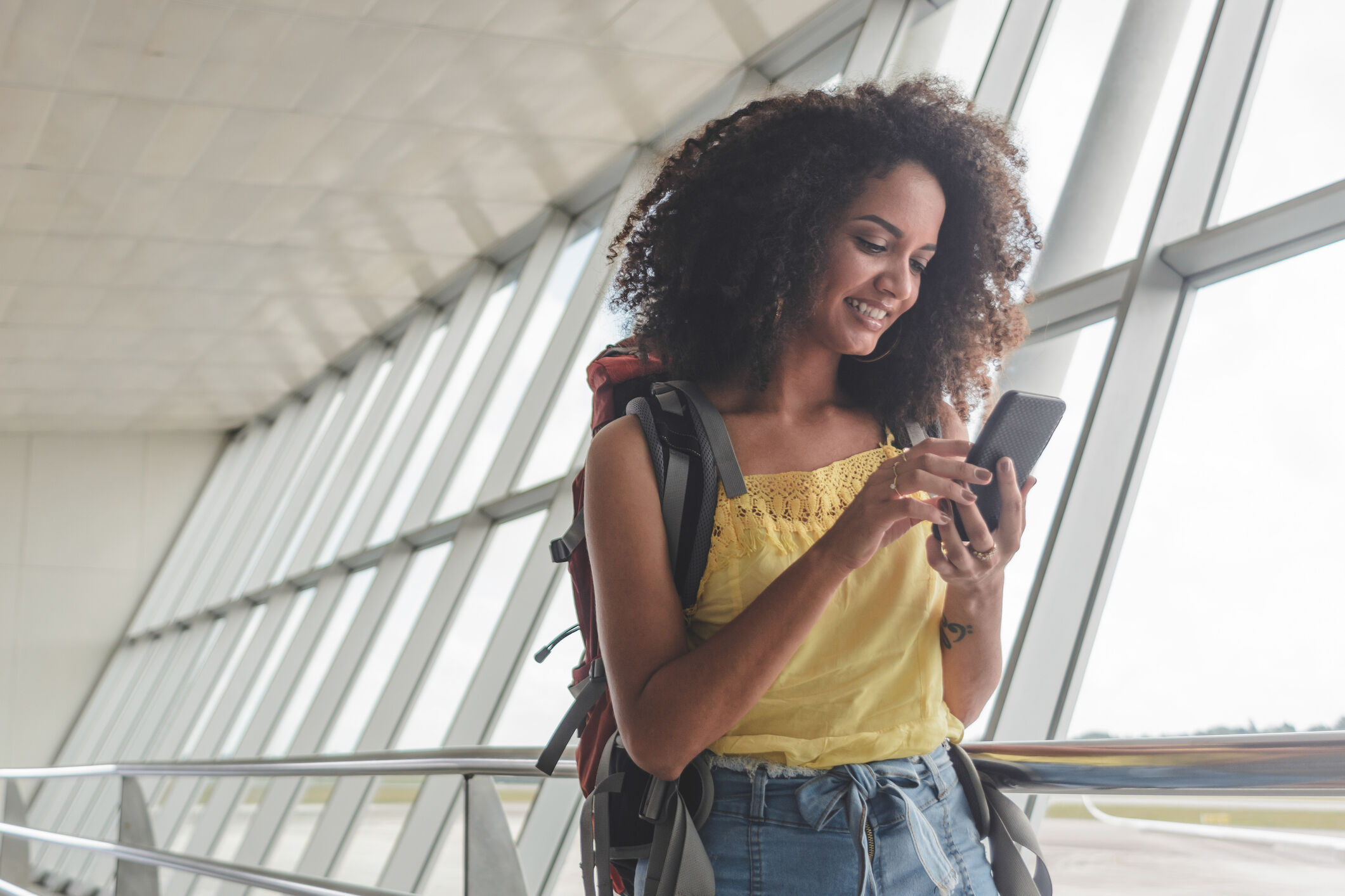 Jeune femme avec sac &agrave; dos v&eacute;rifiant son horaire d'embarquement &agrave; l'a&eacute;roport