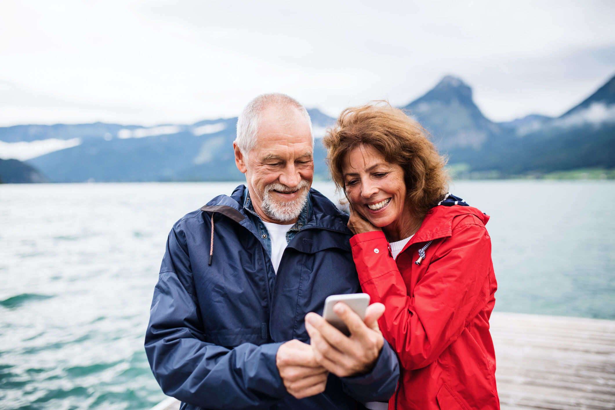 Joyeux couple de personnes &acirc;g&eacute;es debout au bord du lac dans la nature en vacances, &agrave; l'aide d'un smartphone.