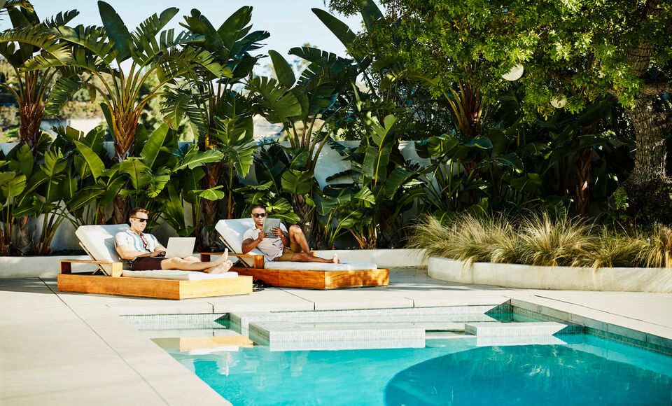 2 hommes travaillant sur ordinateur portable et tablette num&eacute;rique tout en se relaxant au bord de la piscine